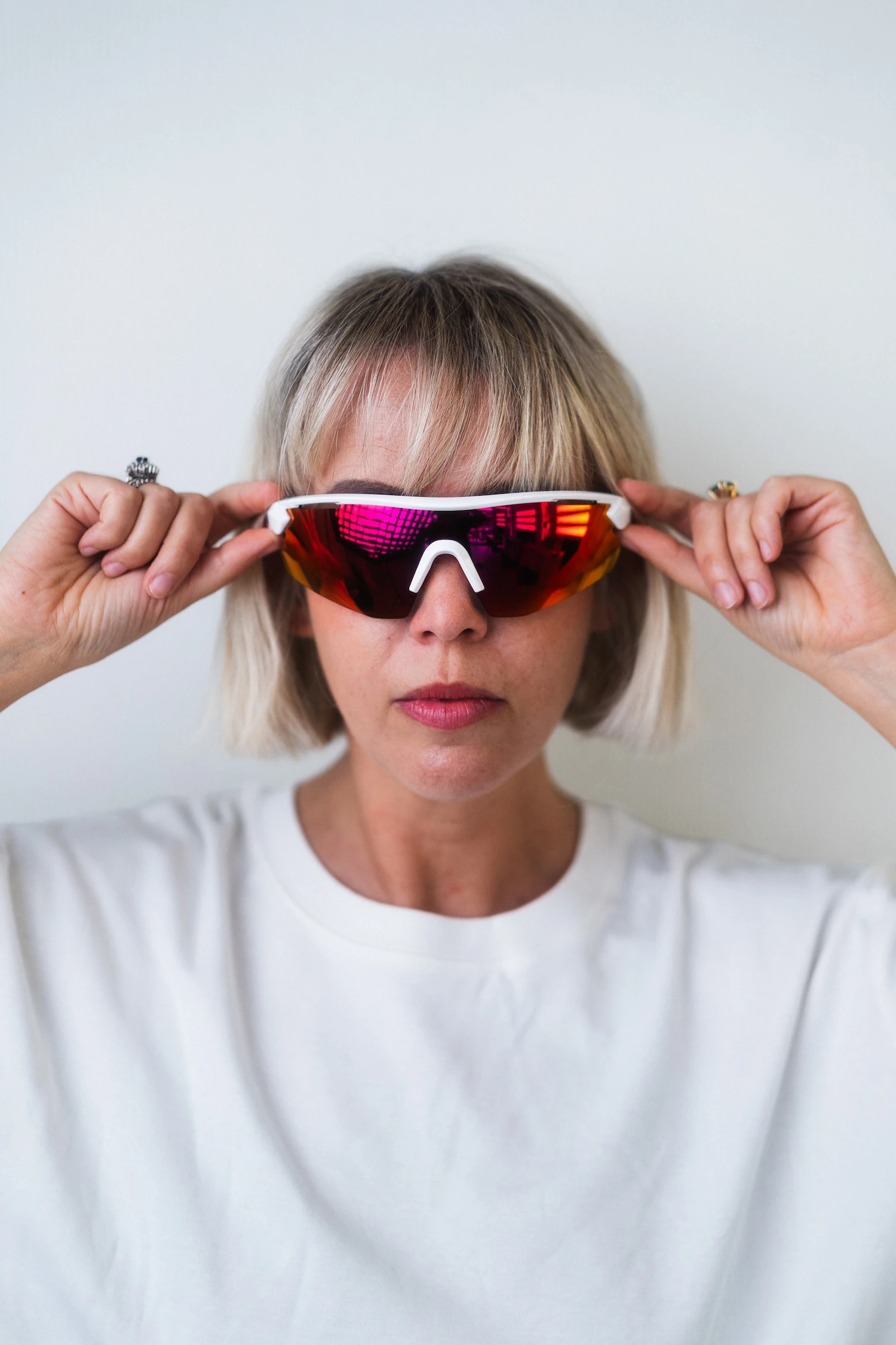 Donna bionda indossa occhiali da sole sportivi a mascherina con lenti specchiate rosse e montatura bianca