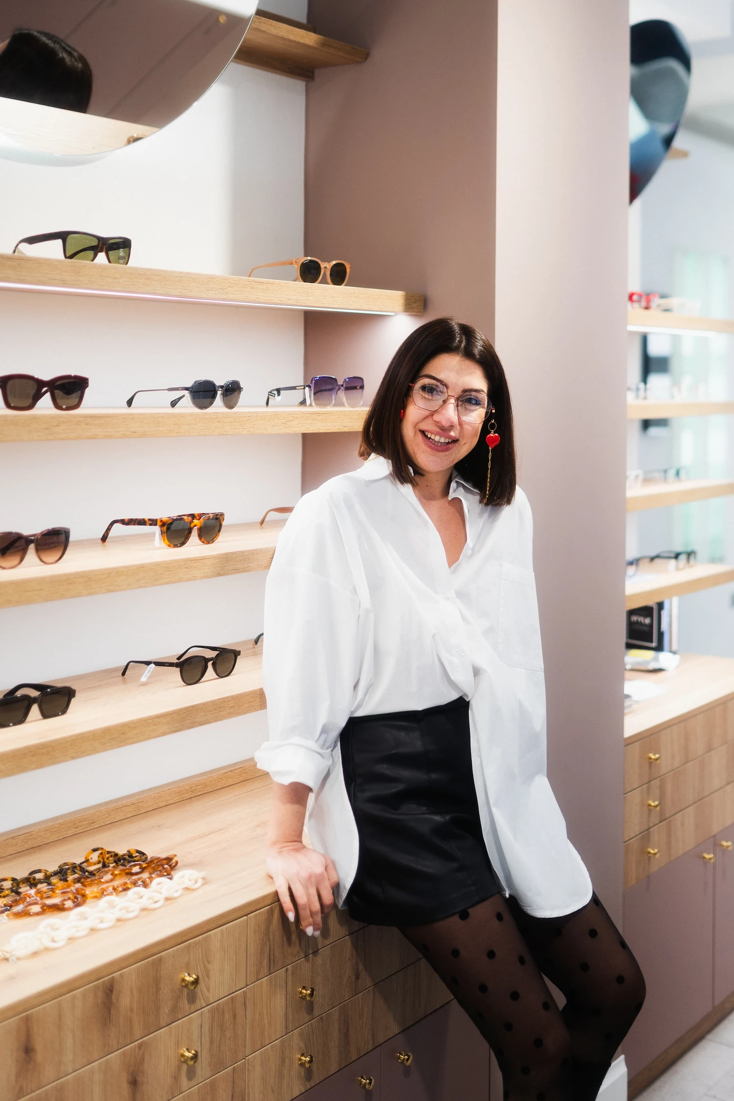 Ottica sorridente appoggiata al bancone del negozio con occhiali da vista in metallo sottile