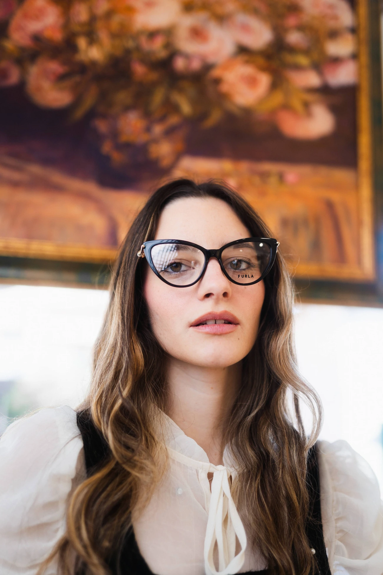 Donna elegante con occhiali da vista neri forma cat-eye davanti a un dipinto classico